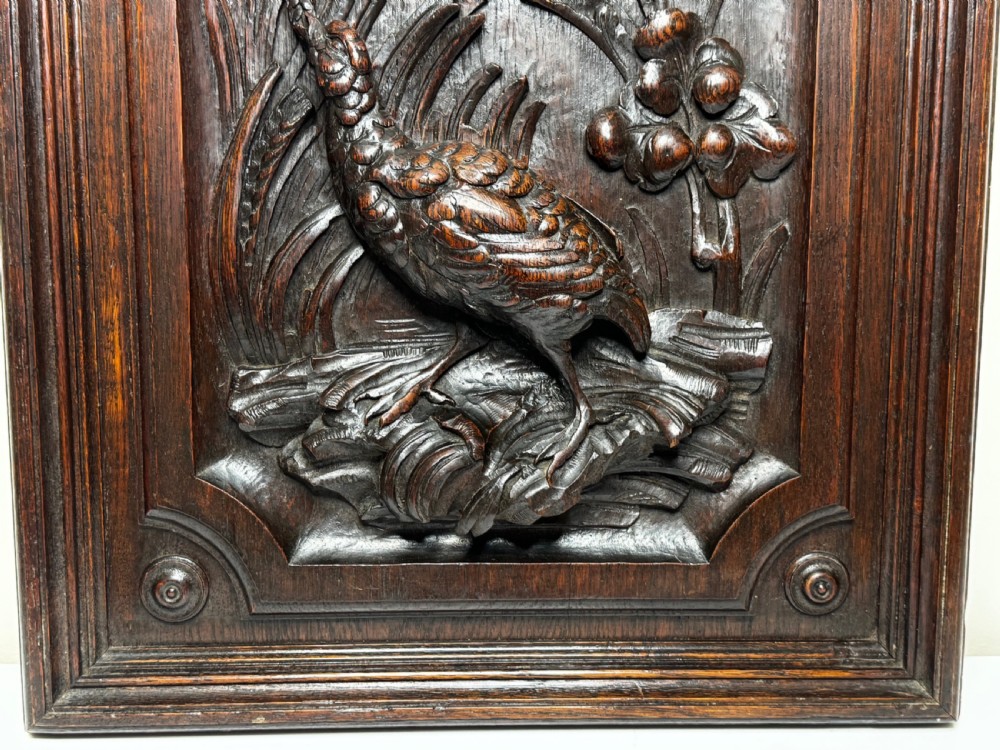 A dark oak relief carving depicting a game bird standing among reeds and oak leaves with acorns inside a moulded frame. View VII