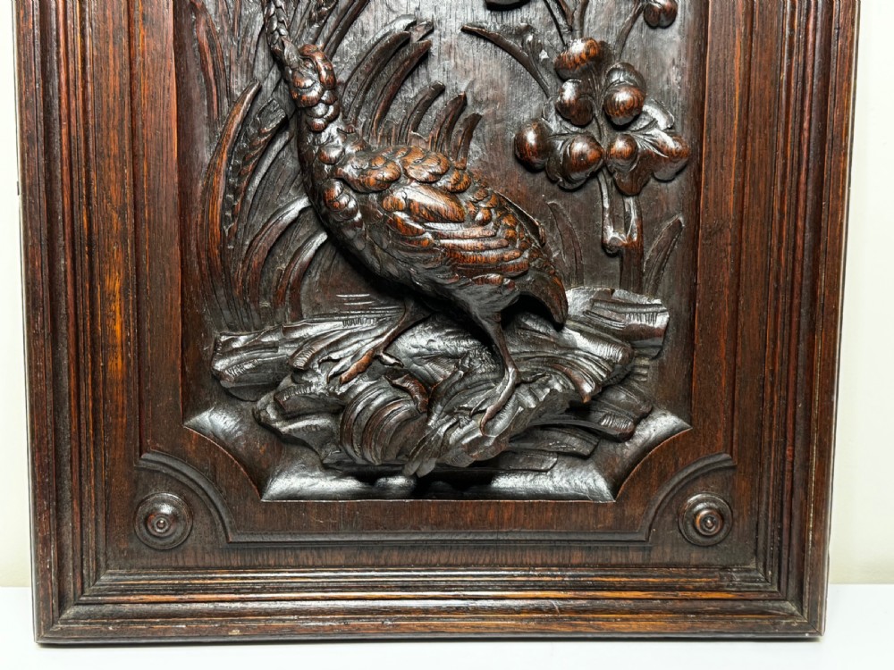 A dark oak relief carving depicting a game bird standing among reeds and oak leaves with acorns inside a moulded frame. View VIII