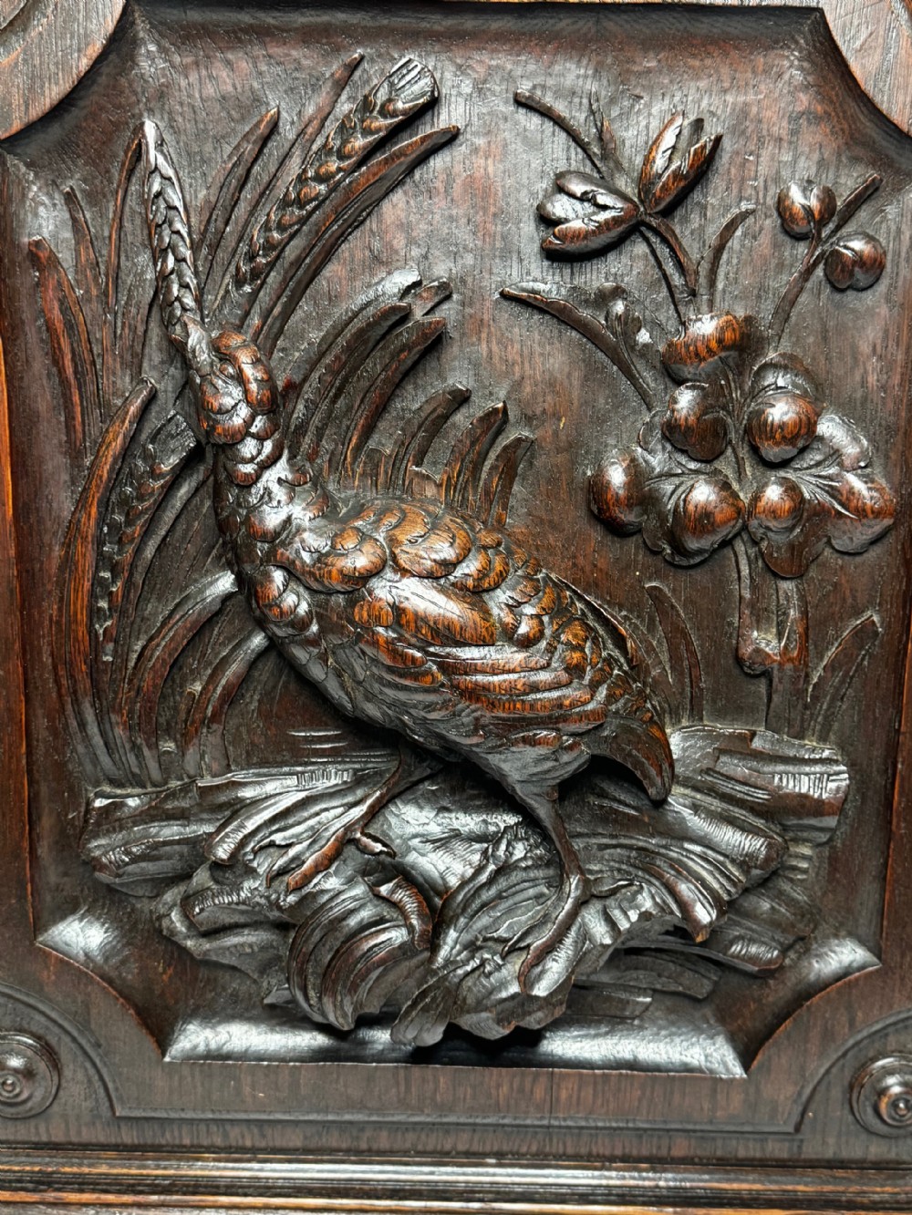 A dark oak relief carving depicting a game bird standing among reeds and oak leaves with acorns inside a moulded frame. View IX