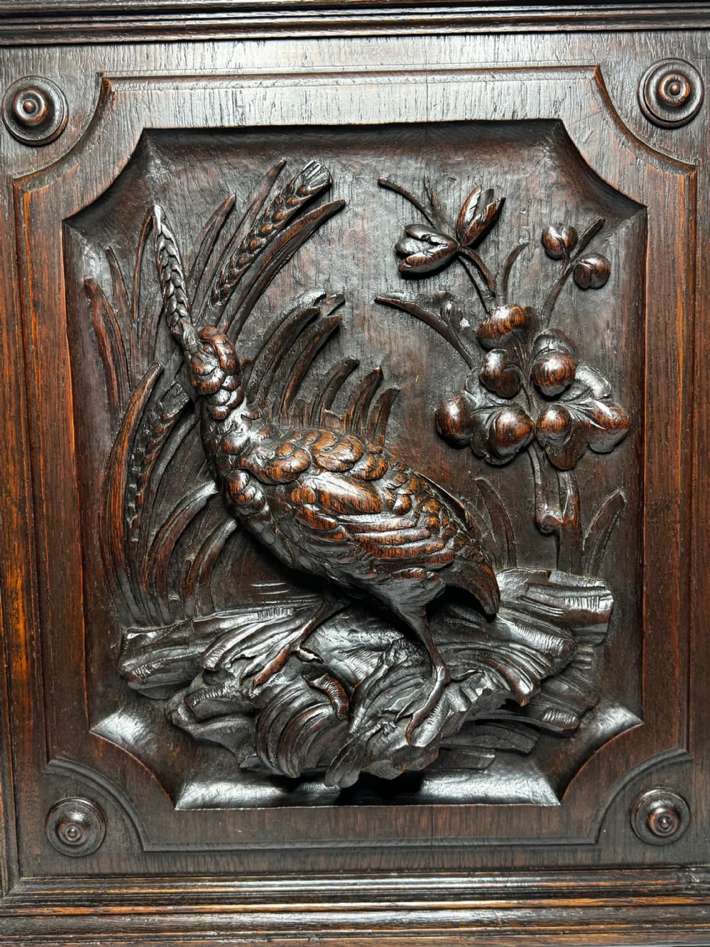 A dark oak relief carving depicting a game bird standing among reeds and oak leaves with acorns inside a moulded frame. View XII