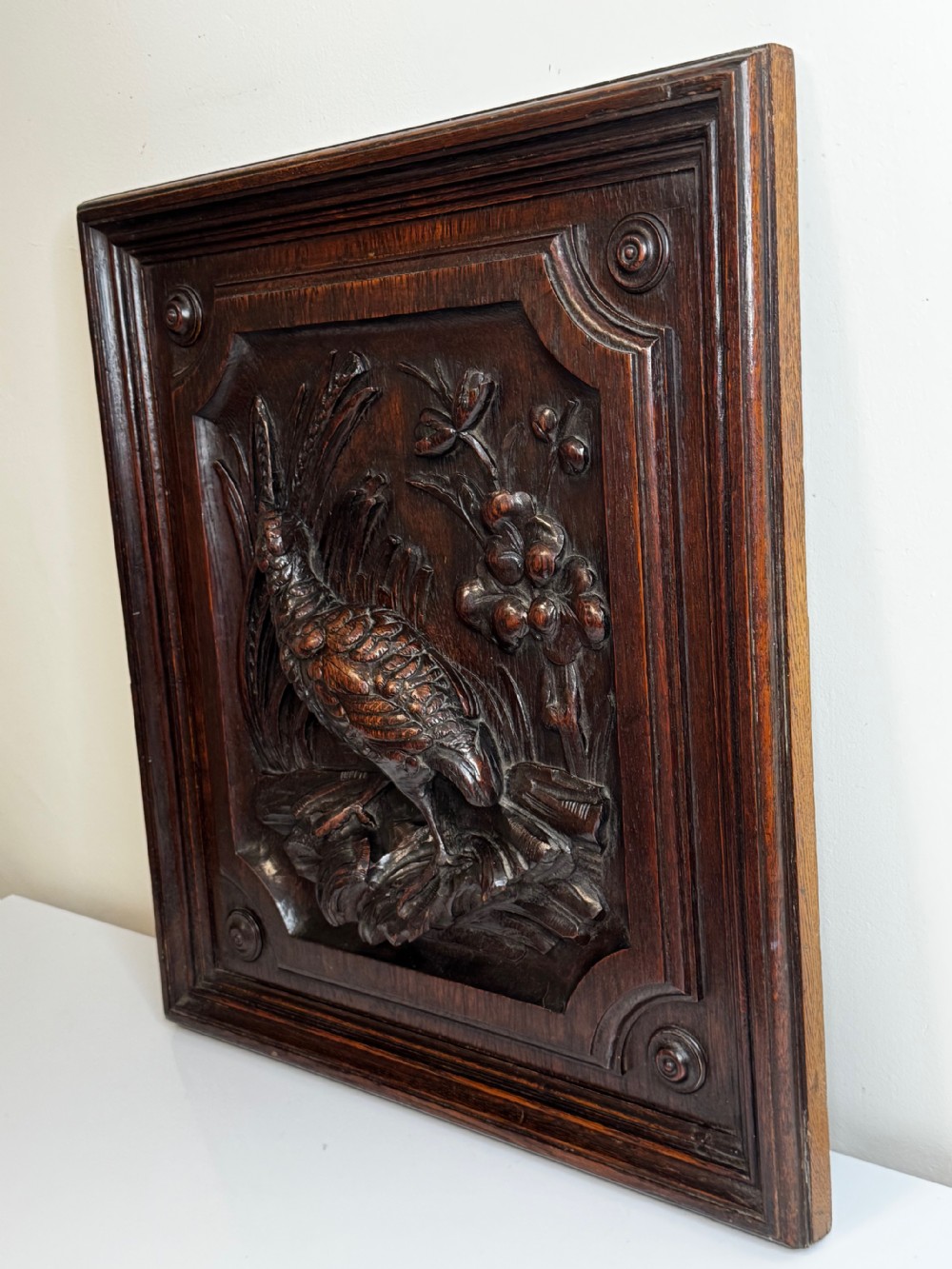 A dark oak relief carving depicting a game bird standing among reeds and oak leaves with acorns inside a moulded frame. View XIII