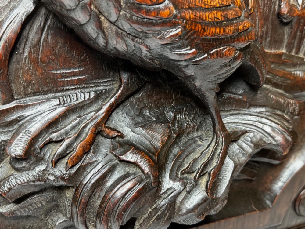 A dark oak relief carving depicting a game bird standing among reeds and oak leaves with acorns inside a moulded frame. View XX