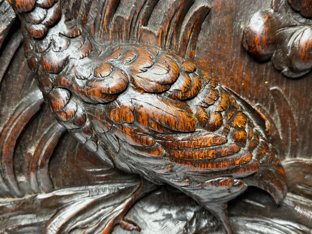A dark oak relief carving depicting a game bird standing among reeds and oak leaves with acorns inside a moulded frame. View XXI
