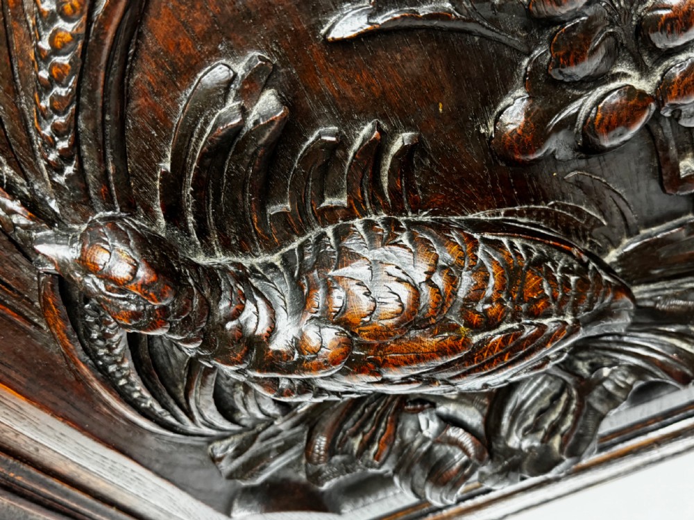 A dark oak relief carving depicting a game bird standing among reeds and oak leaves with acorns inside a moulded frame. View XXII