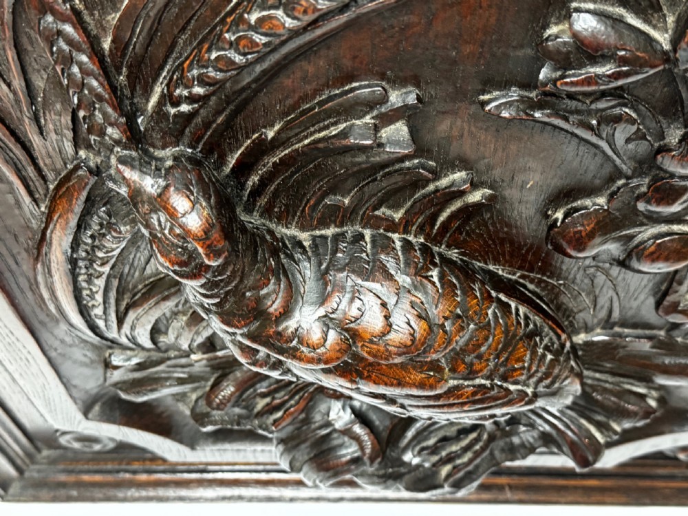 A dark oak relief carving depicting a game bird standing among reeds and oak leaves with acorns inside a moulded frame. View XXIII
