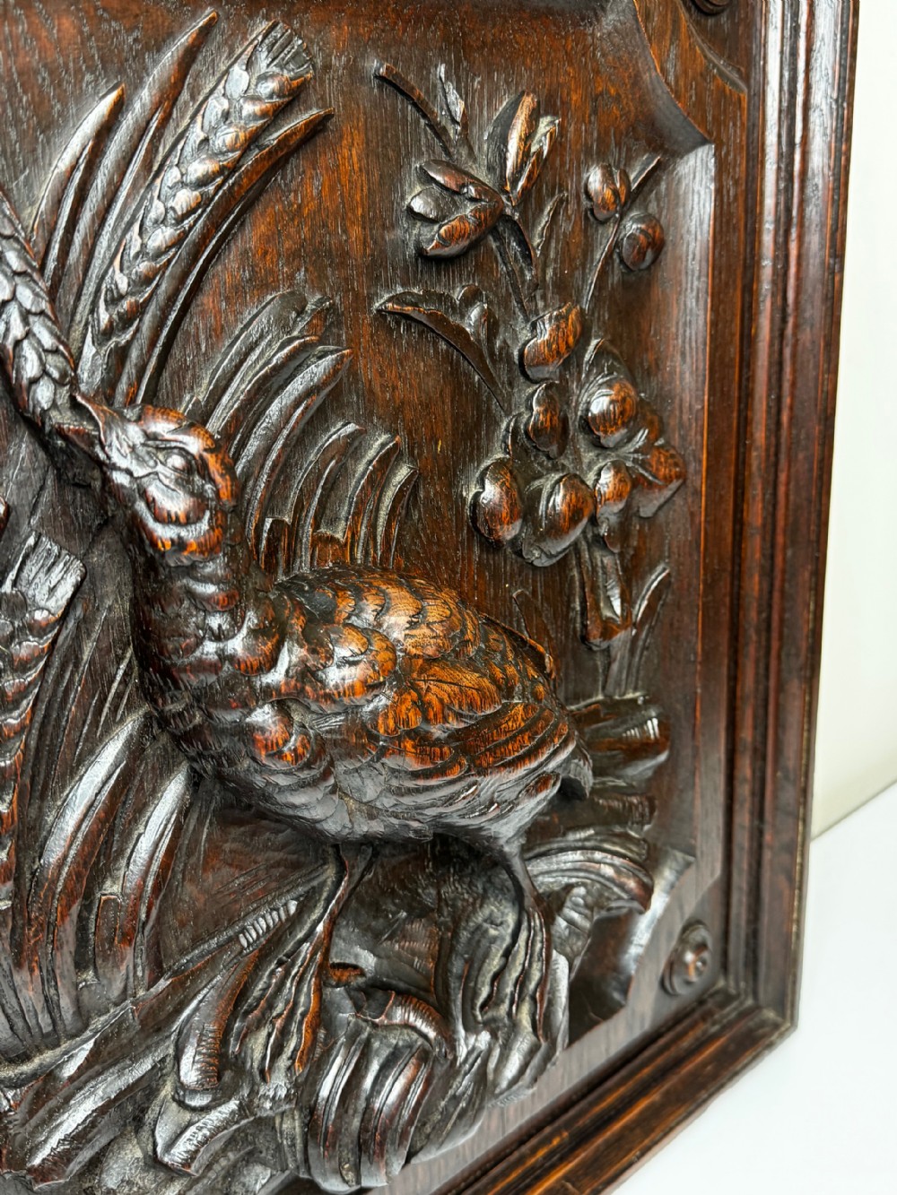 A dark oak relief carving depicting a game bird standing among reeds and oak leaves with acorns inside a moulded frame. View XXIX
