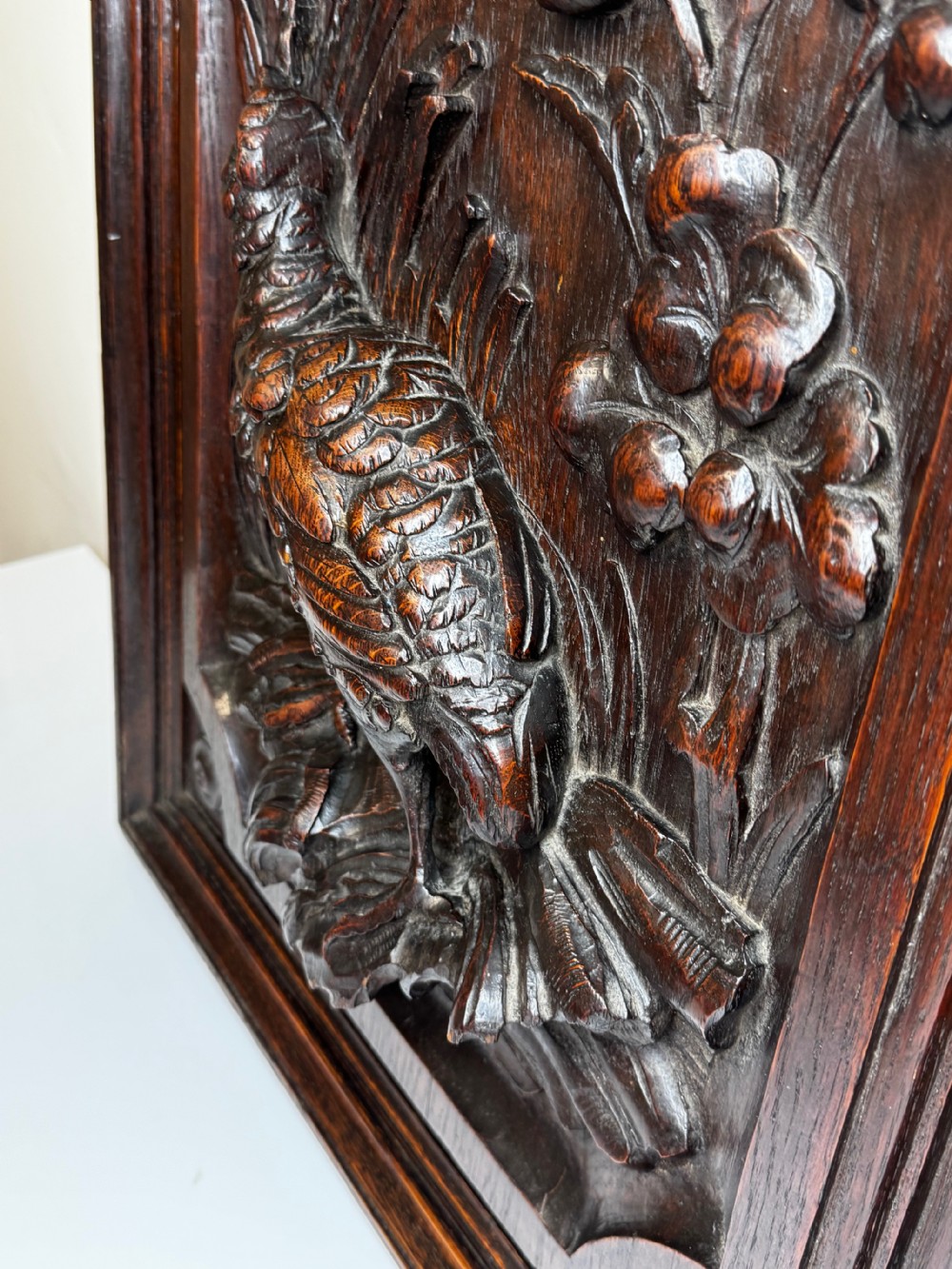 A dark oak relief carving depicting a game bird standing among reeds and oak leaves with acorns inside a moulded frame. View XXX