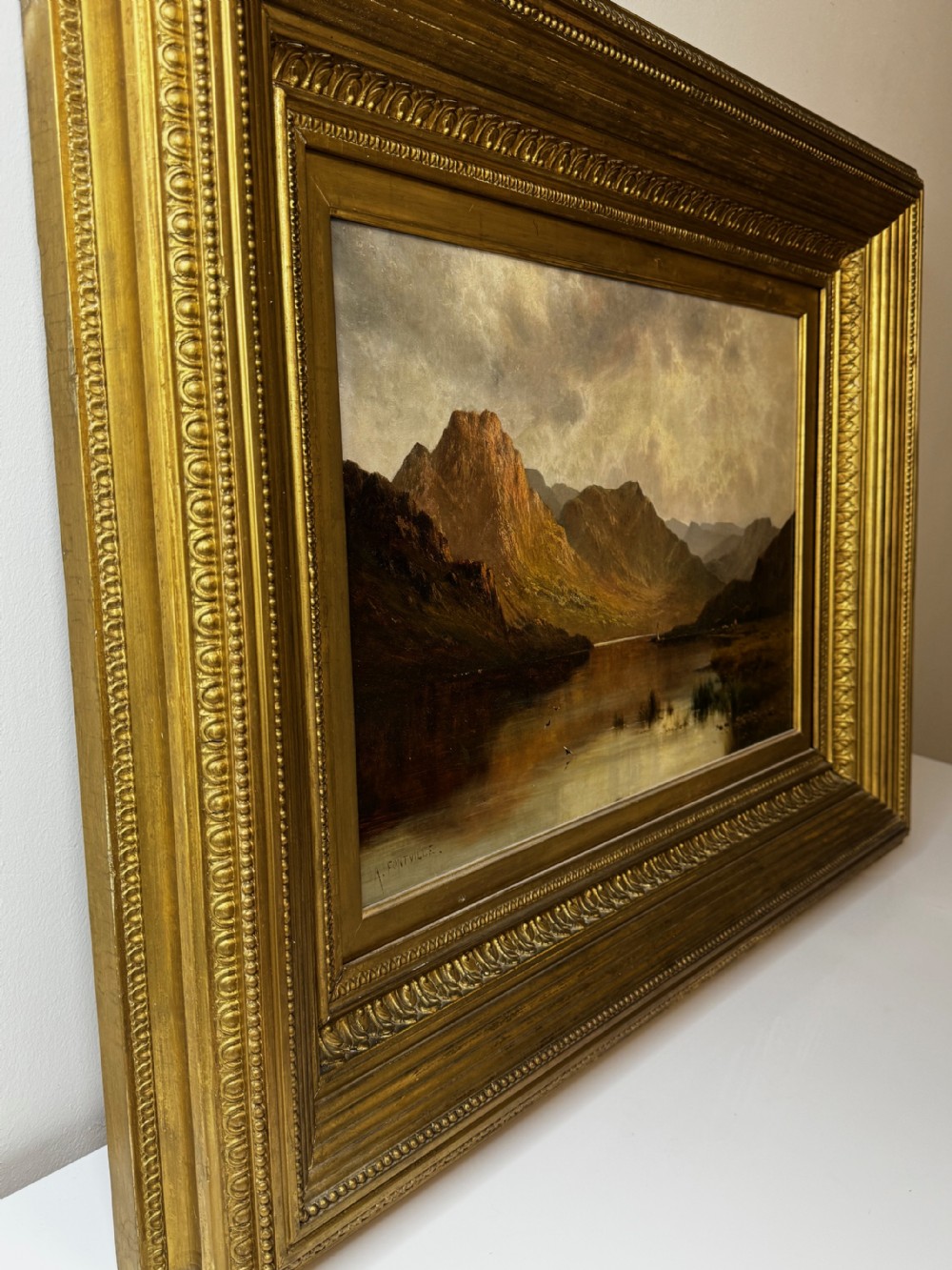 A Victorian landscape oil painting depicting Lake Windermere with mountains in the background, set within a heavy multi-moulded gold frame. View X