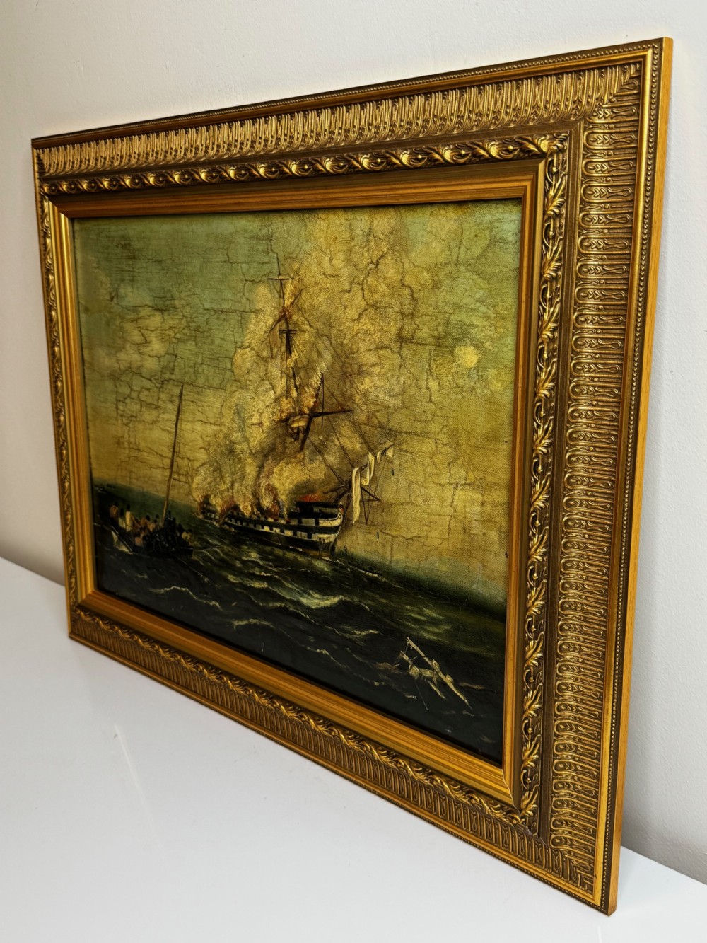 A framed 19th-century style maritime oil painting on canvas depicting a ship engulfed in flames on choppy seas, set within an ornate gilded frame. View V