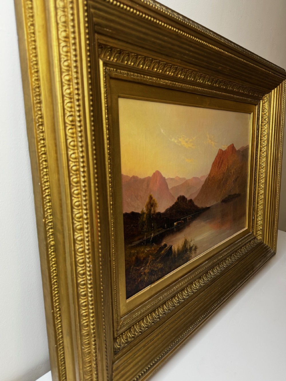 A Victorian oil painting depicting a lake landscape at sunset framed in a heavily moulded gilded frame. View VI