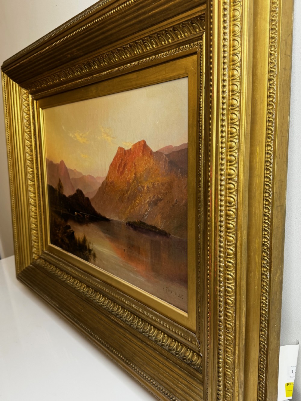 A Victorian oil painting depicting a lake landscape at sunset framed in a heavily moulded gilded frame. View X