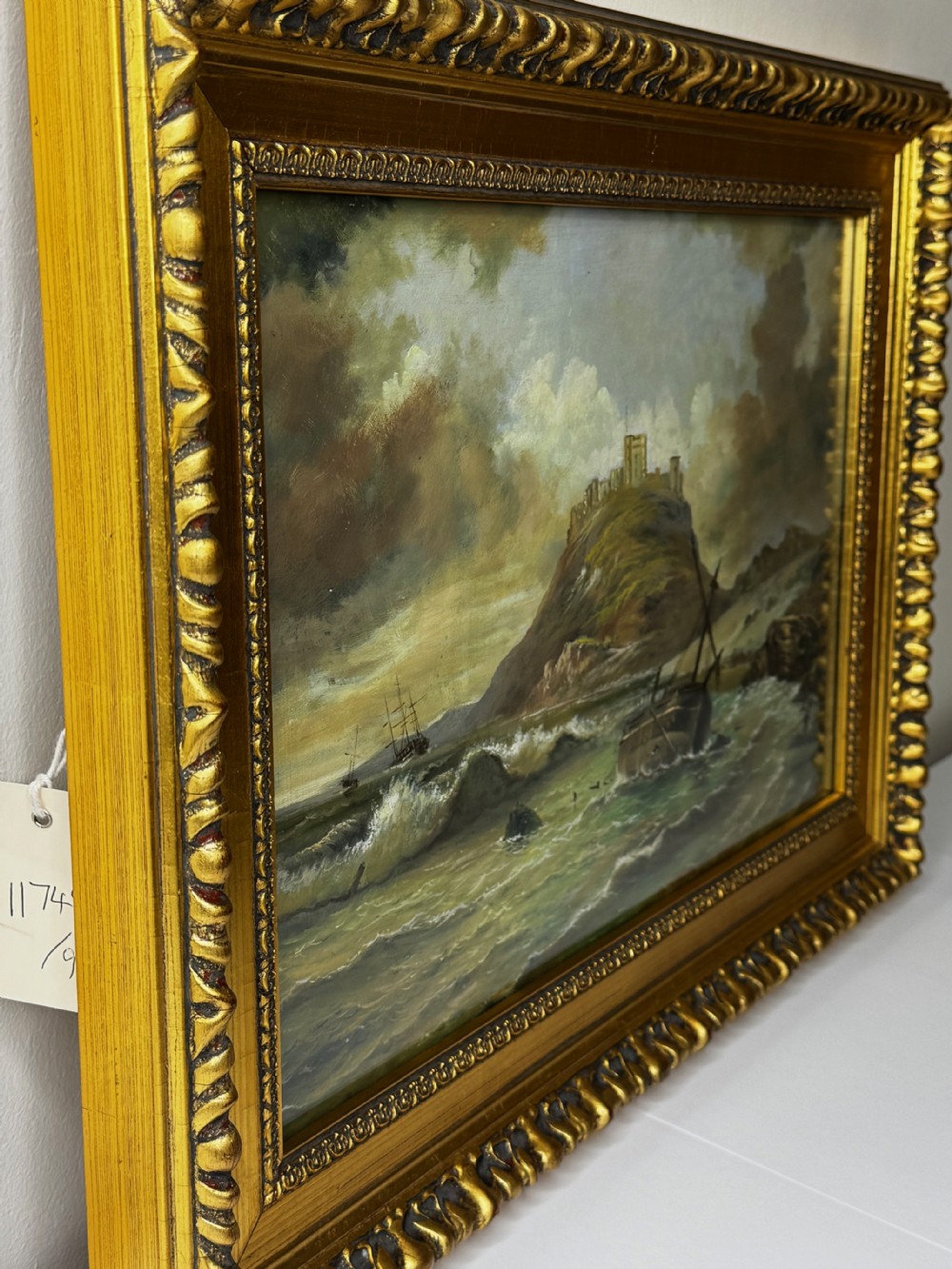 A Victorian oil painting depicting a coastal shipwreck near Bamburgh Castle under a cloudy sky, enclosed in a heavily gilded frame. View XI