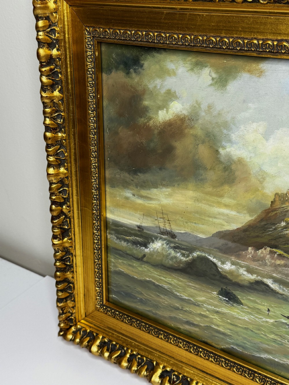 A Victorian oil painting depicting a coastal shipwreck near Bamburgh Castle under a cloudy sky, enclosed in a heavily gilded frame. View XII