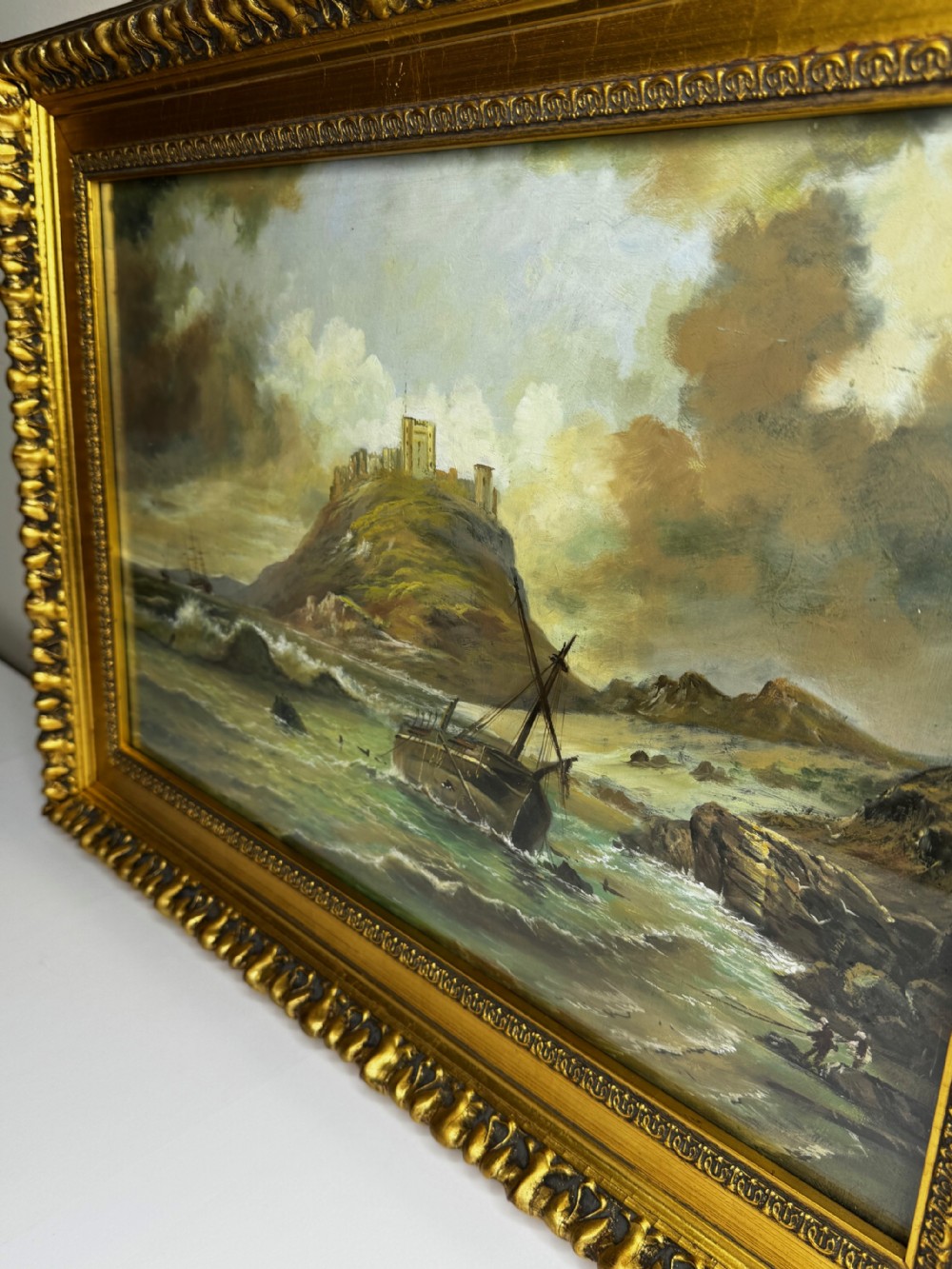A Victorian oil painting depicting a coastal shipwreck near Bamburgh Castle under a cloudy sky, enclosed in a heavily gilded frame. View XIII