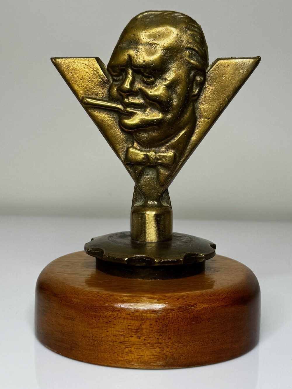 A cast gilt bronze car mascot depicting Winston Churchill with a cigar against a V for victory motif, mounted on a round wooden base. View II