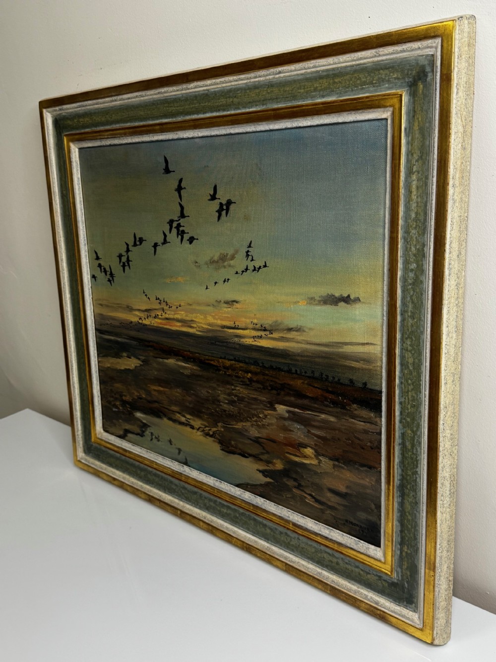 Framed oil painting depicting a skein of geese in flight over coastal marshlands at dusk. View IV