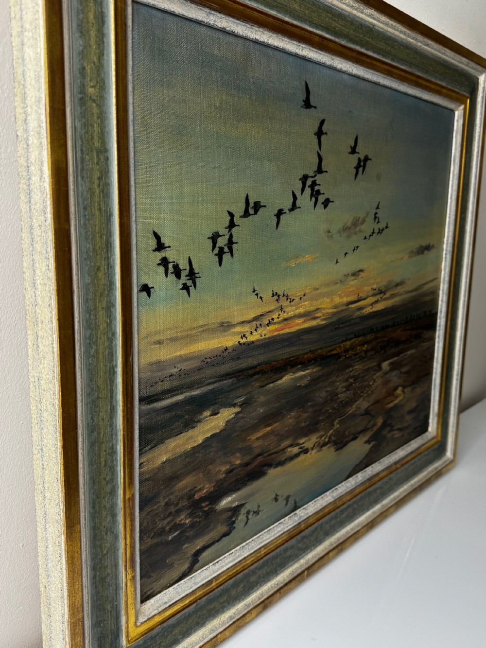 Framed oil painting depicting a skein of geese in flight over coastal marshlands at dusk. View IX