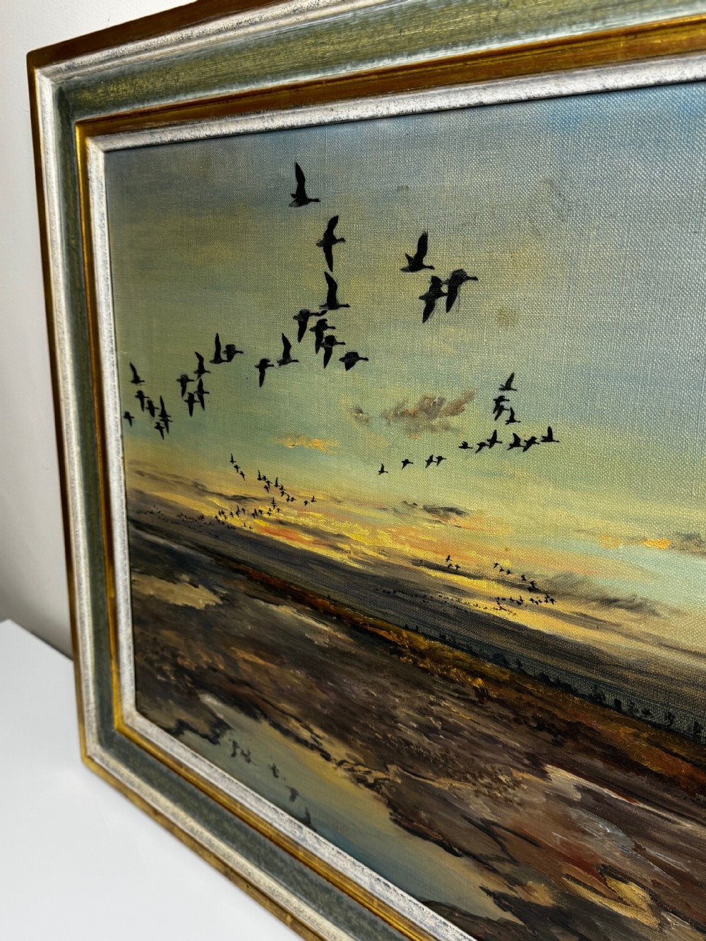 Framed oil painting depicting a skein of geese in flight over coastal marshlands at dusk. View XII