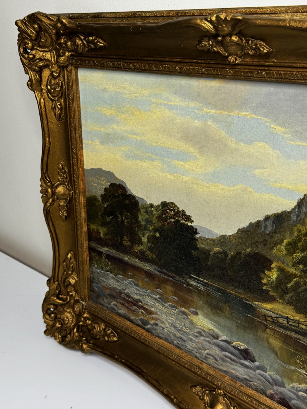 A 19th-century Victorian oil painting depicting a river running through a mountainous Welsh landscape, enclosed in an ornate gold gilt frame. View VI