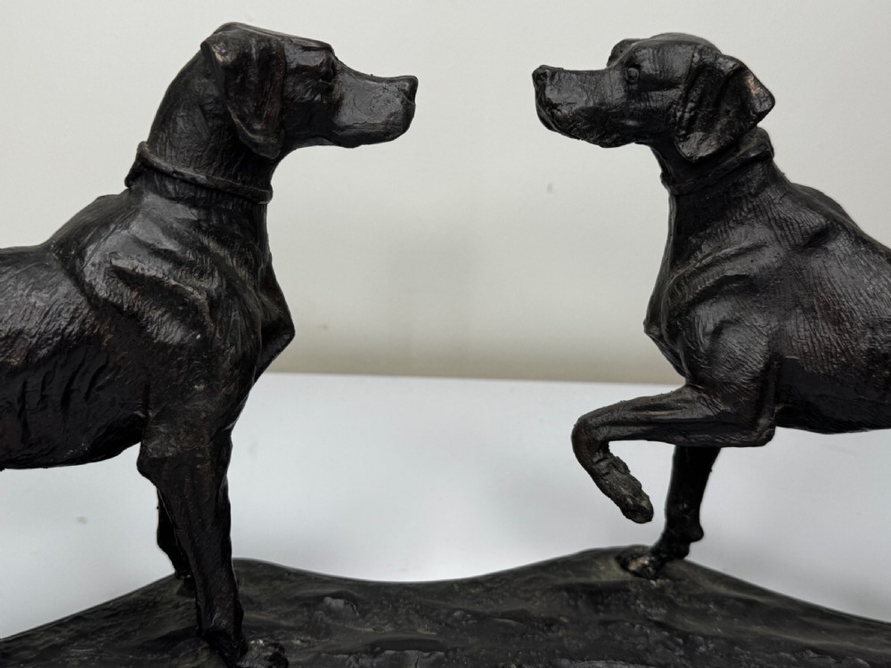 A dark patinated bronze sculpture depicting two hunting hound dogs in active poses on an integral naturalistic base. View IX