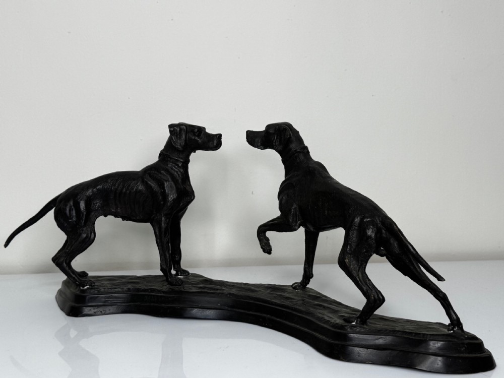 A dark patinated bronze sculpture depicting two hunting hound dogs in active poses on an integral naturalistic base. View XXIV