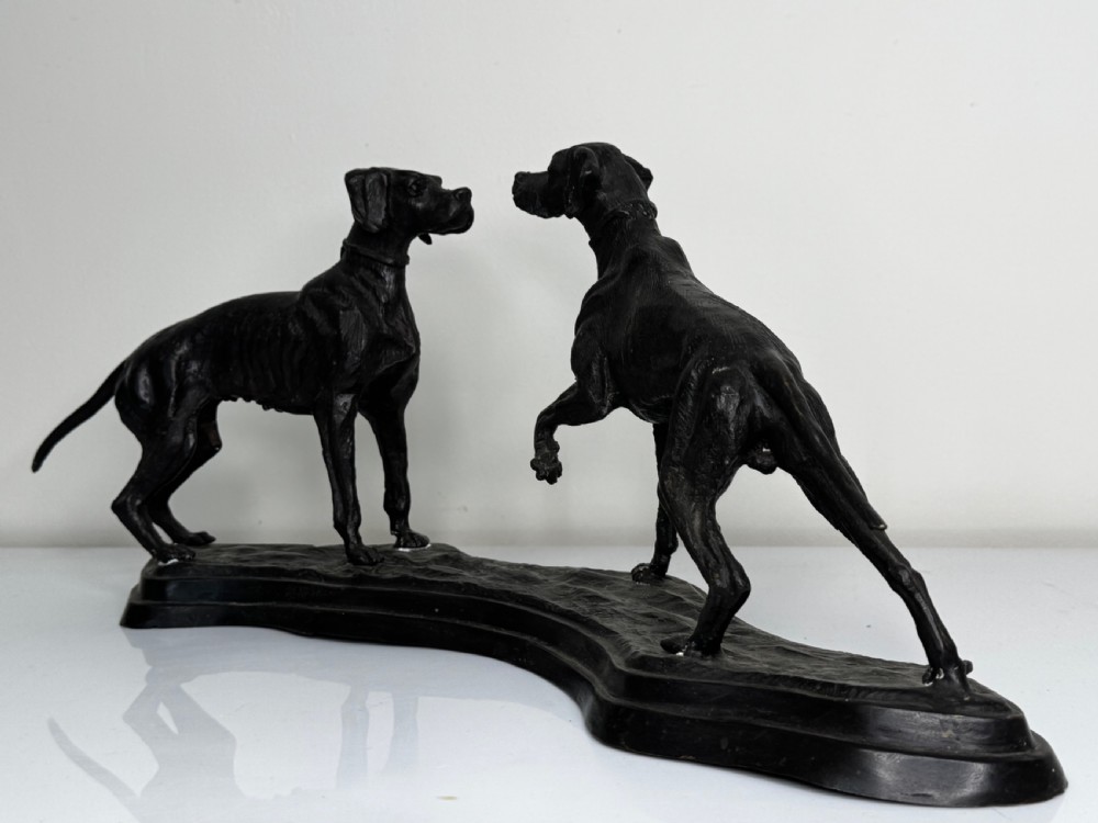 A dark patinated bronze sculpture depicting two hunting hound dogs in active poses on an integral naturalistic base. View XXVI