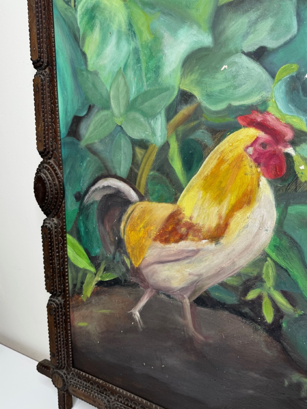 An oil painting depicting a yellow and red cockerel amidst dense green leaves, set within a carved dark wood frame with extended corner joints. View IV