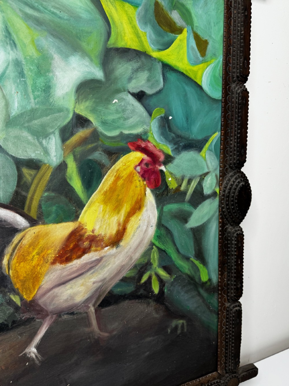 An oil painting depicting a yellow and red cockerel amidst dense green leaves, set within a carved dark wood frame with extended corner joints. View VI