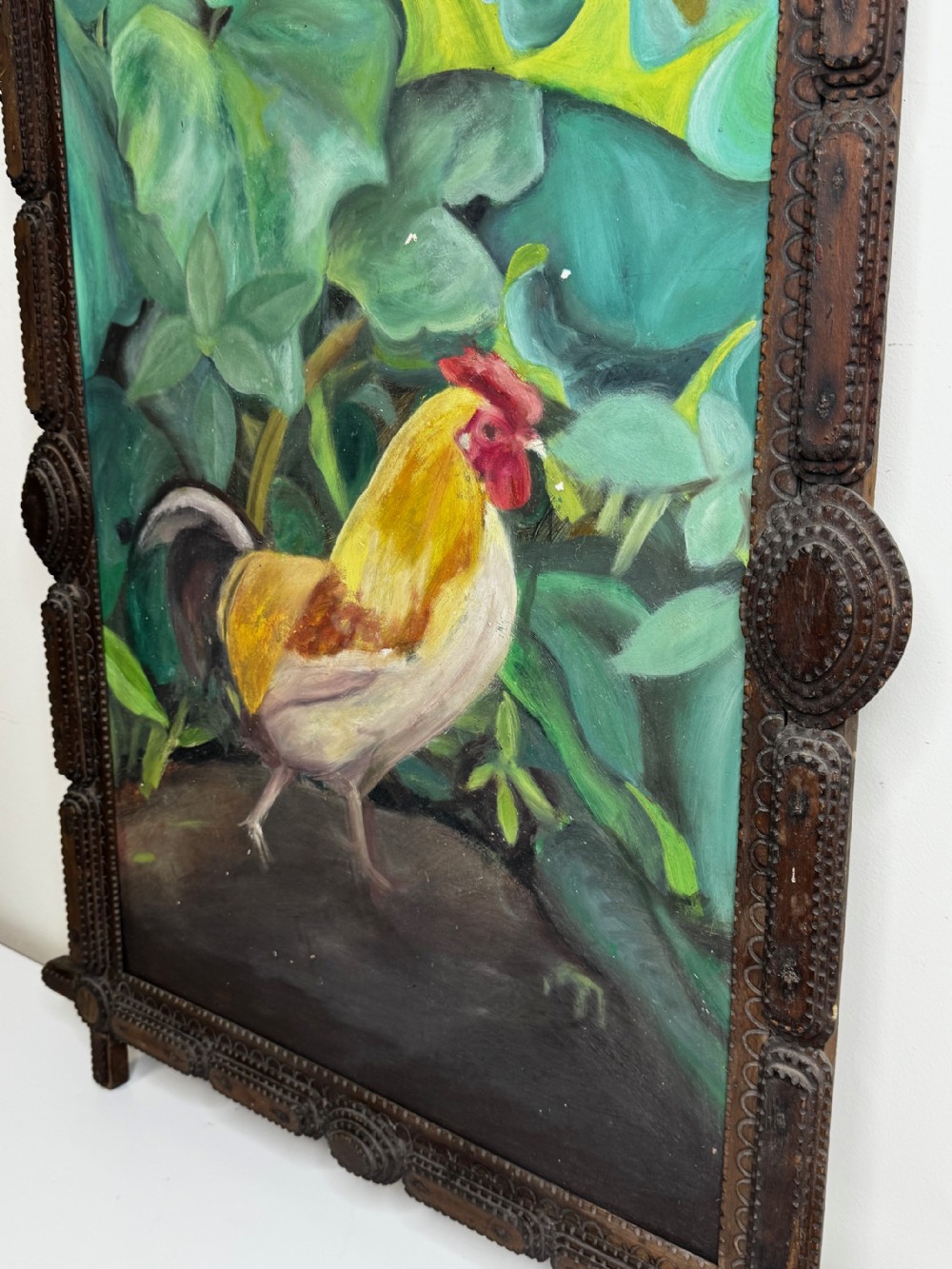 An oil painting depicting a yellow and red cockerel amidst dense green leaves, set within a carved dark wood frame with extended corner joints. View XI
