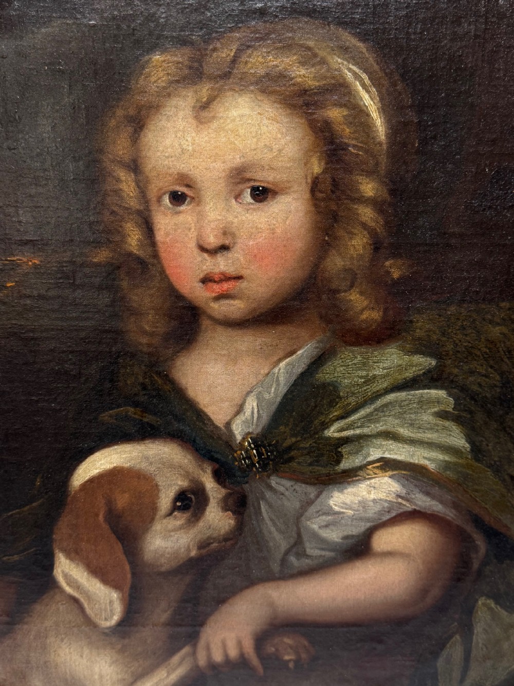 An oval seventeenth-century style oil portrait depicting a young child resting a hand on a King Charles Spaniel puppy, housed in a molded gilt frame. View II
