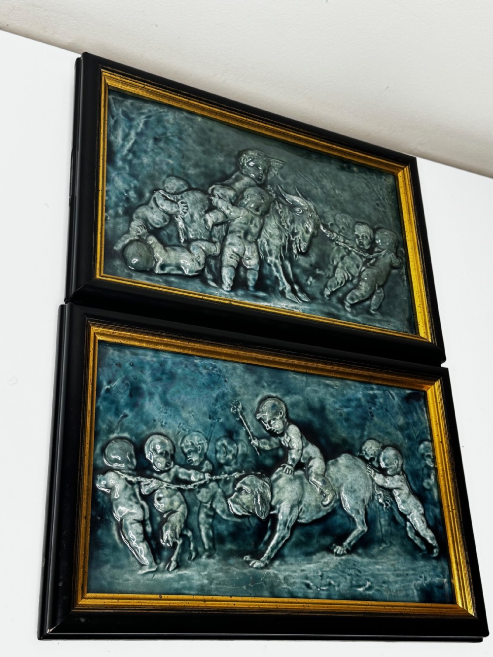 A pair of rectangular Arts and Crafts earthenware relief plaques with turquoise glaze displaying scenes of children with a goat and dog set in ebonised frames. View IV