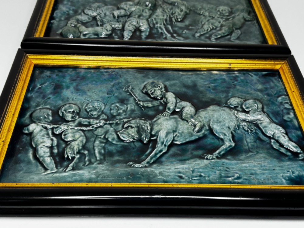 A pair of rectangular Arts and Crafts earthenware relief plaques with turquoise glaze displaying scenes of children with a goat and dog set in ebonised frames. View IX