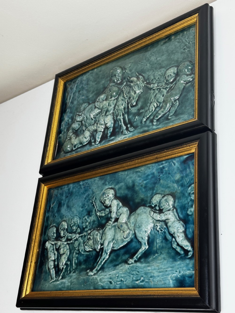 A pair of rectangular Arts and Crafts earthenware relief plaques with turquoise glaze displaying scenes of children with a goat and dog set in ebonised frames. View X