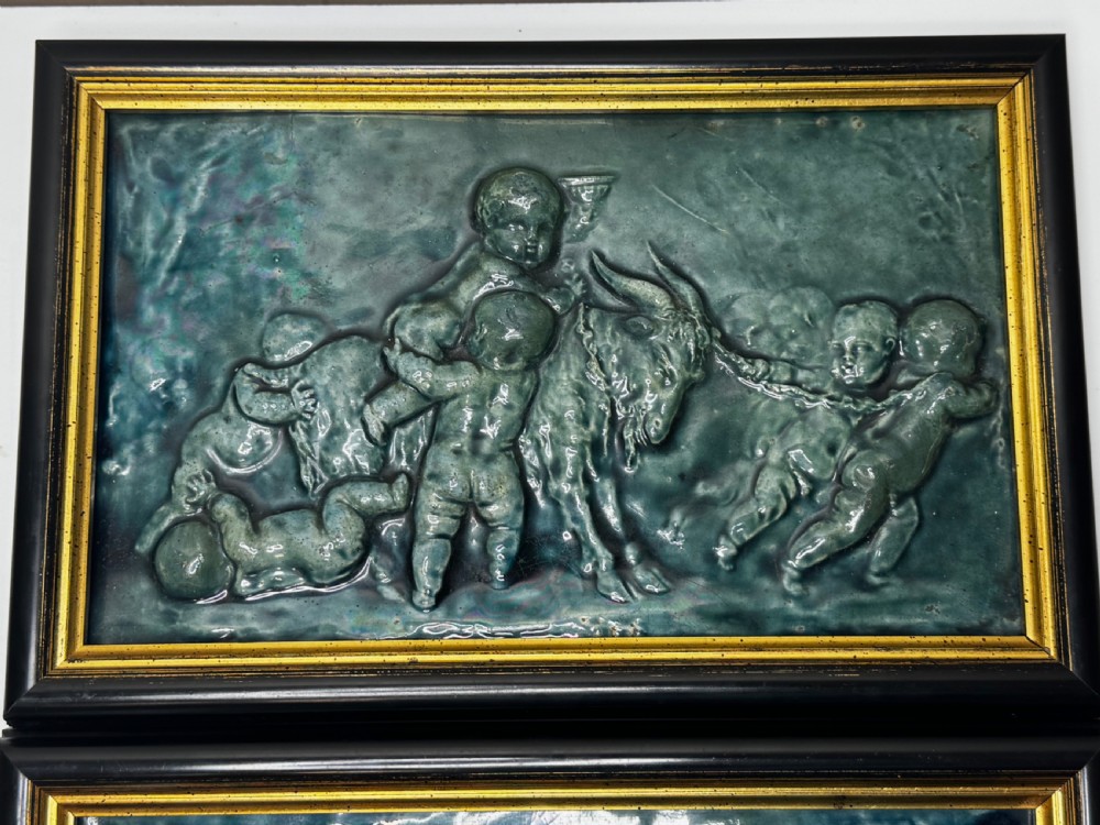 A pair of rectangular Arts and Crafts earthenware relief plaques with turquoise glaze displaying scenes of children with a goat and dog set in ebonised frames. View XVII
