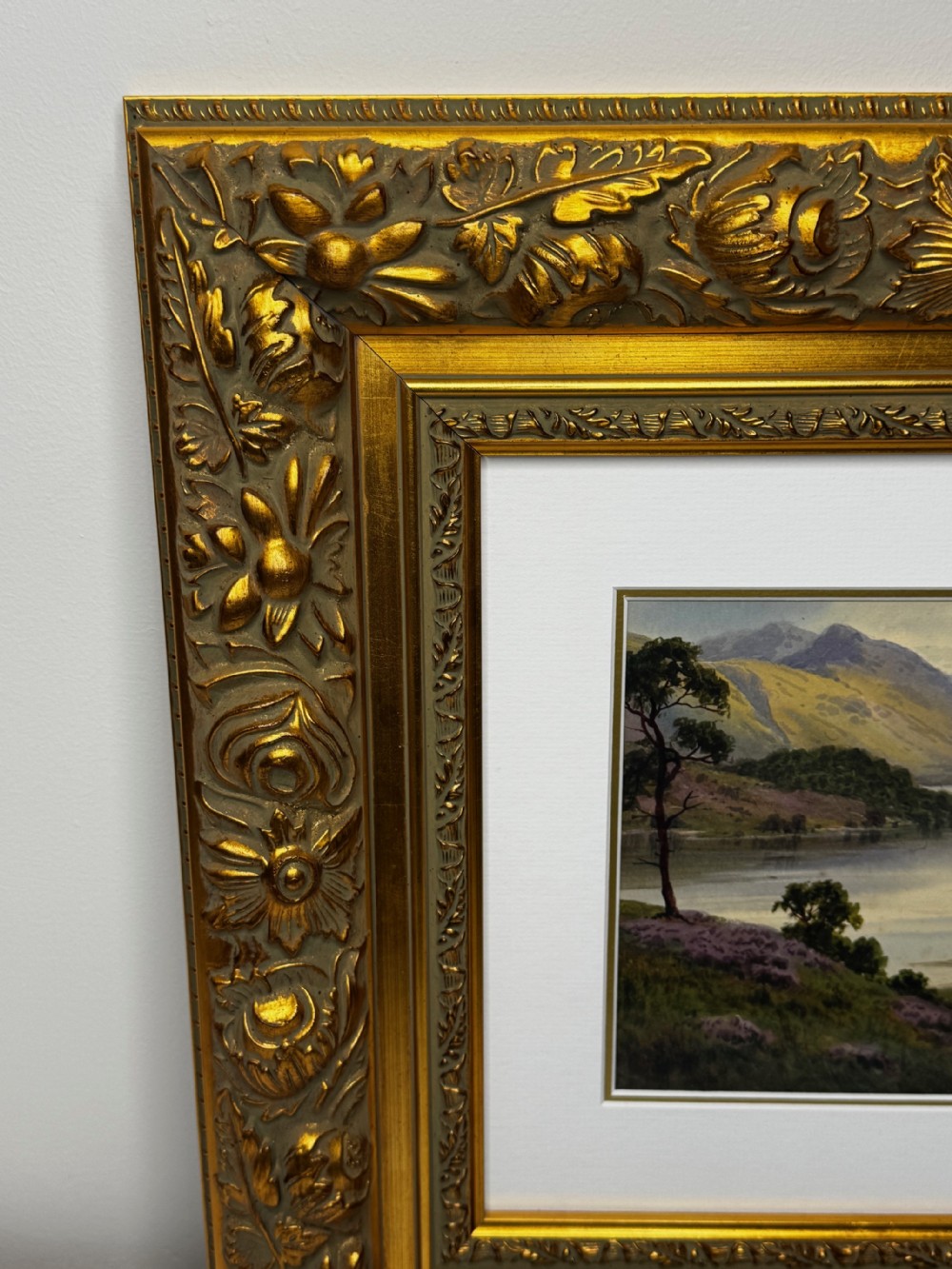 An early 20th-century framed watercolour painting depicting a serene Lake District landscape with a body of water and mountains, framed in a heavy gilt floral moulding. View IX