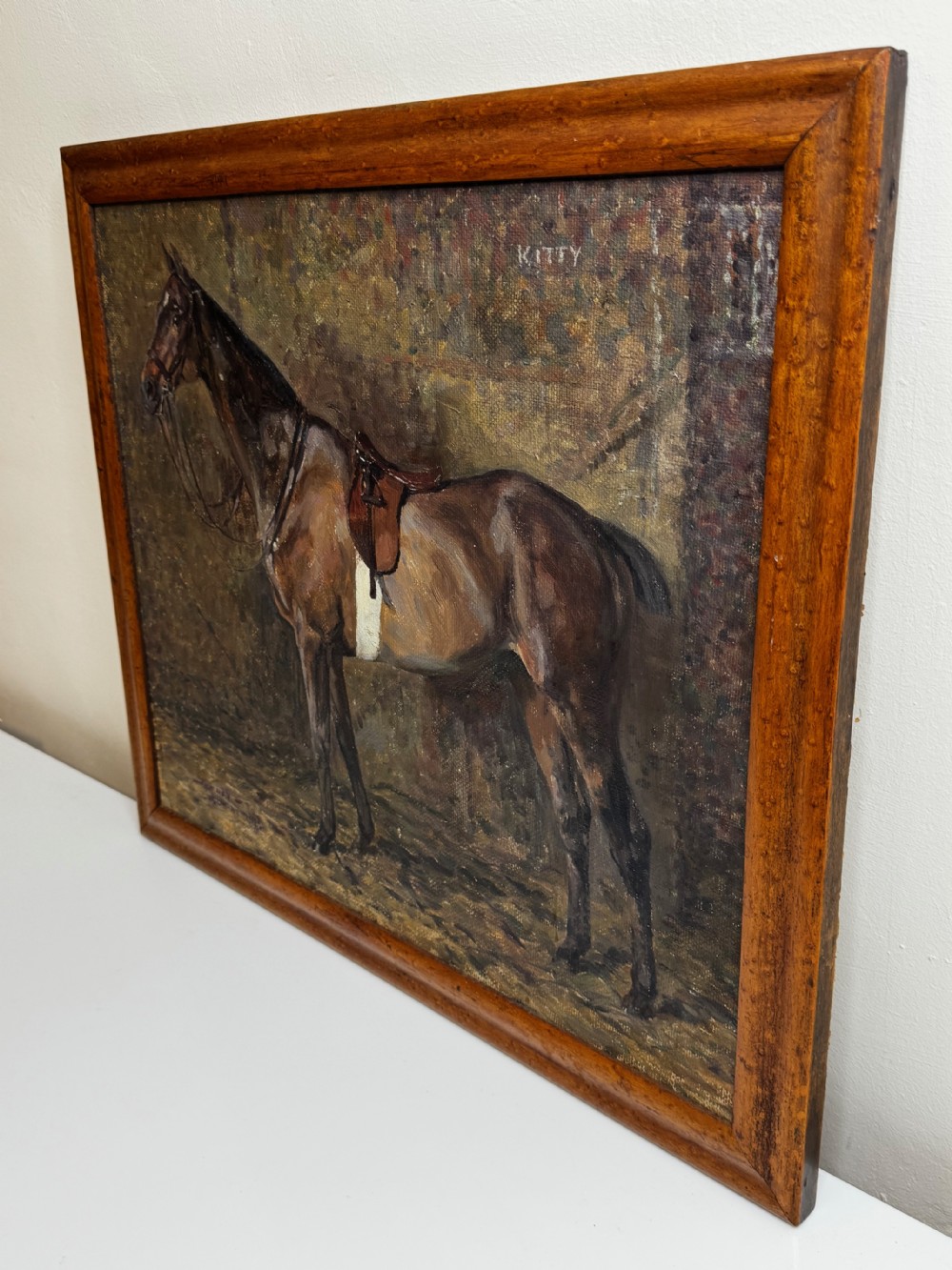 An oil painting framed in wood depicting a saddled brown hunter mare named Kitty standing in profile within a stable setting. View IX