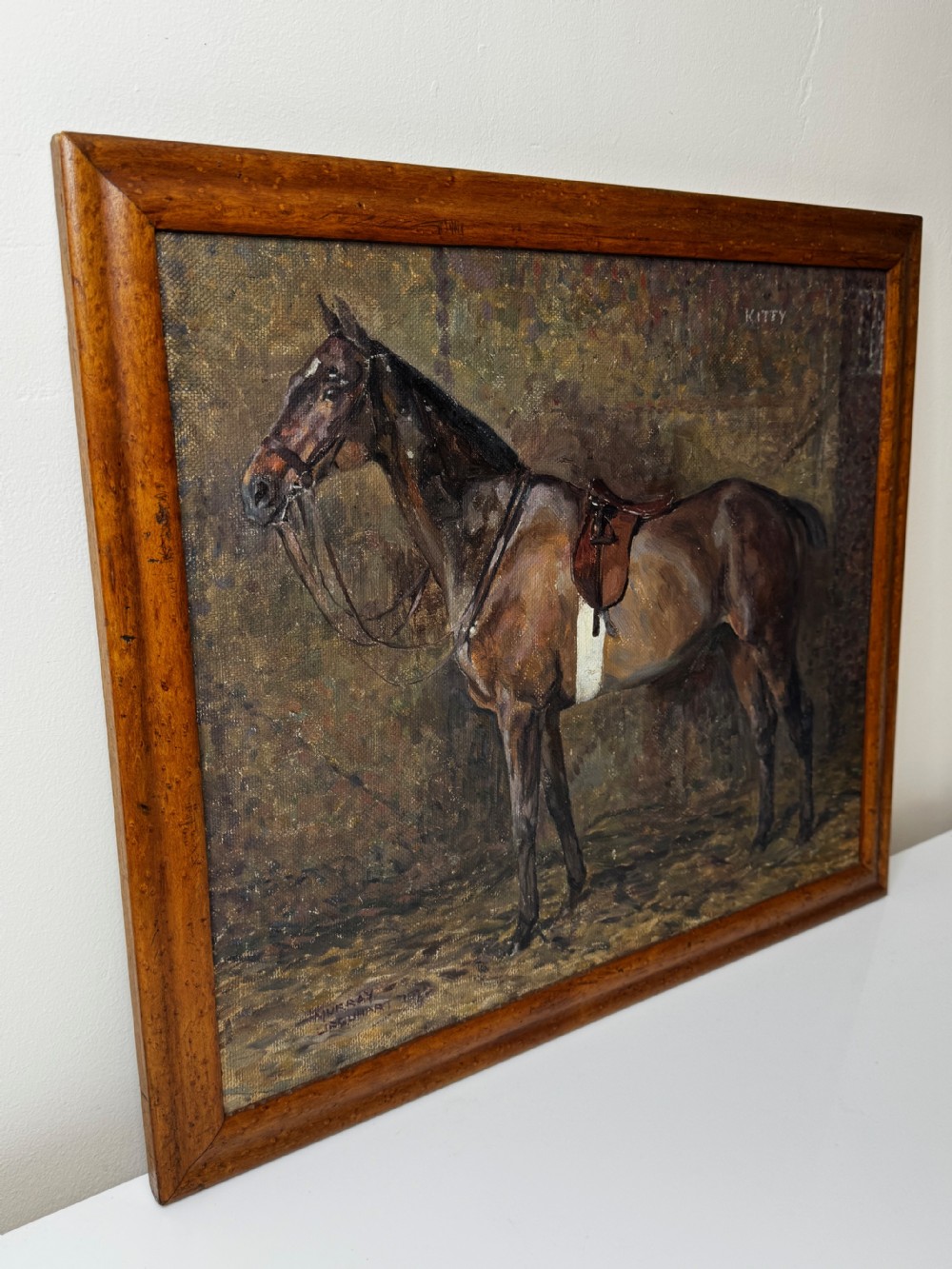 An oil painting framed in wood depicting a saddled brown hunter mare named Kitty standing in profile within a stable setting. View XII