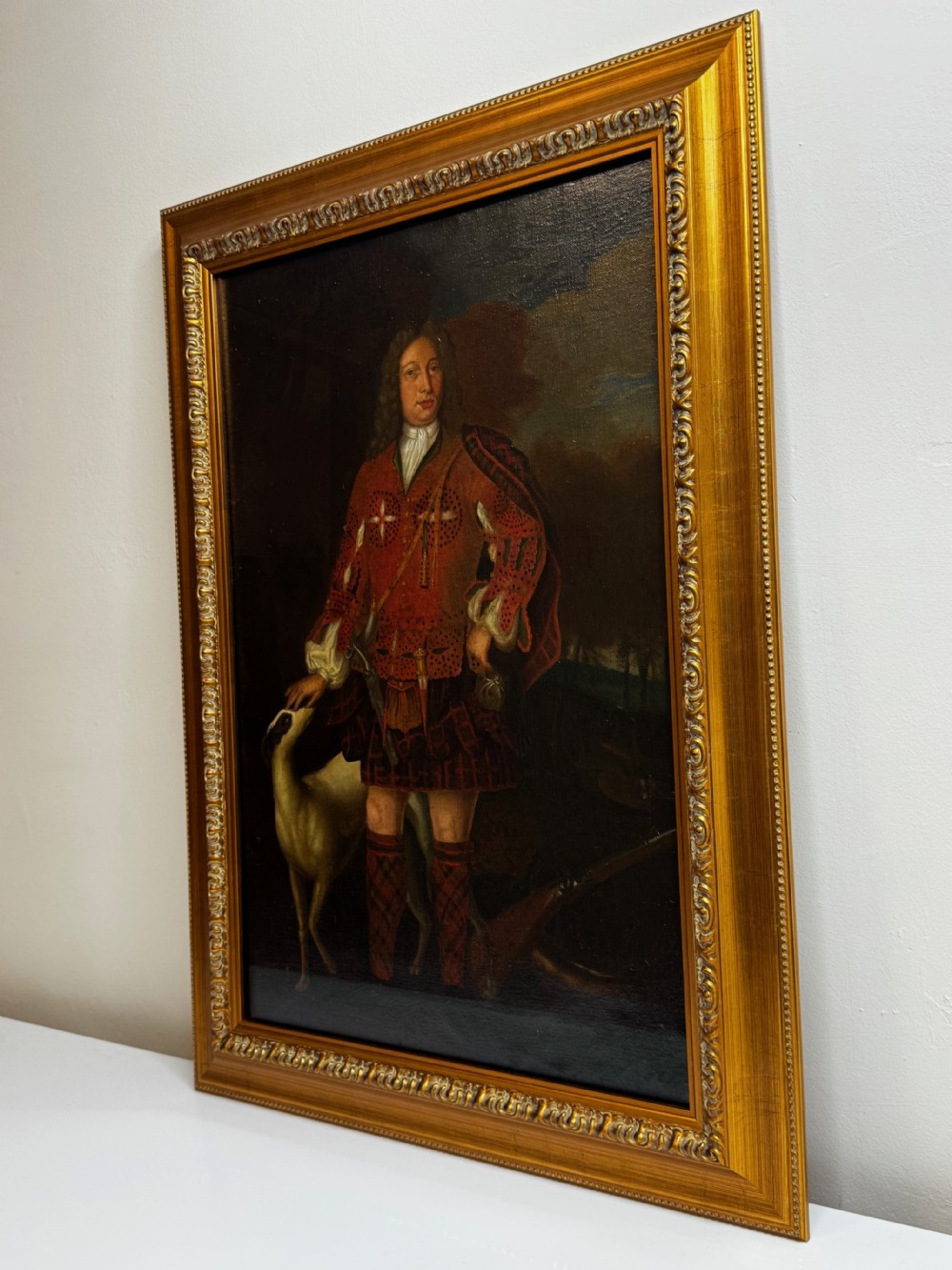 An 18th-century oil painting depicting a Scottish noble standing in tartan attire beside a hunting hound, set within a carved gilt frame. View II