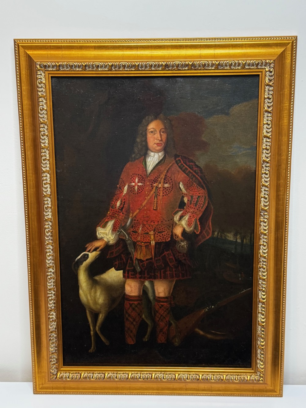 An 18th-century oil painting depicting a Scottish noble standing in tartan attire beside a hunting hound, set within a carved gilt frame. View XIV