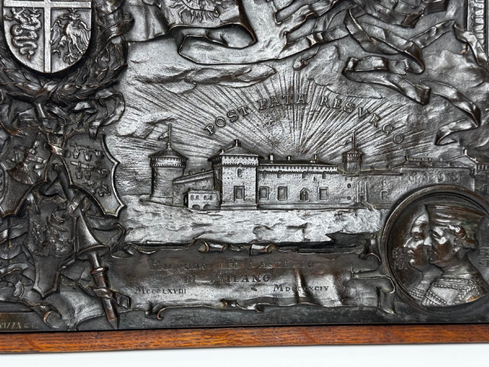 A rectangular dark bronze relief plaque depicting Castello Sforzesco with heraldic coats of arms, mounted inside a wooden frame. View XV