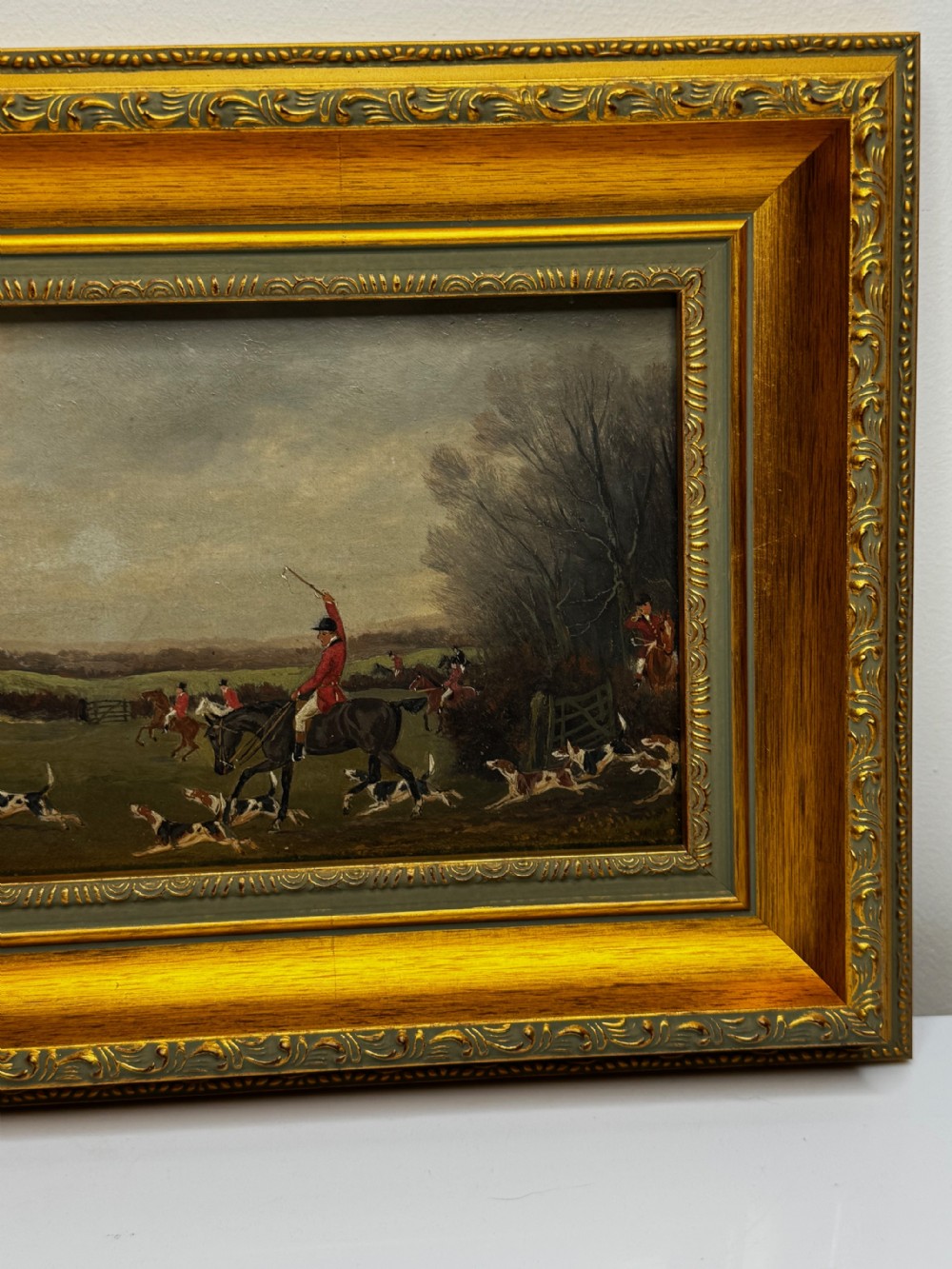 A 19th-century oil painting depicting a traditional fox hunting scene with huntsmen on horseback and hounds in an open landscape, enclosed in an ornate gilded frame. View VI