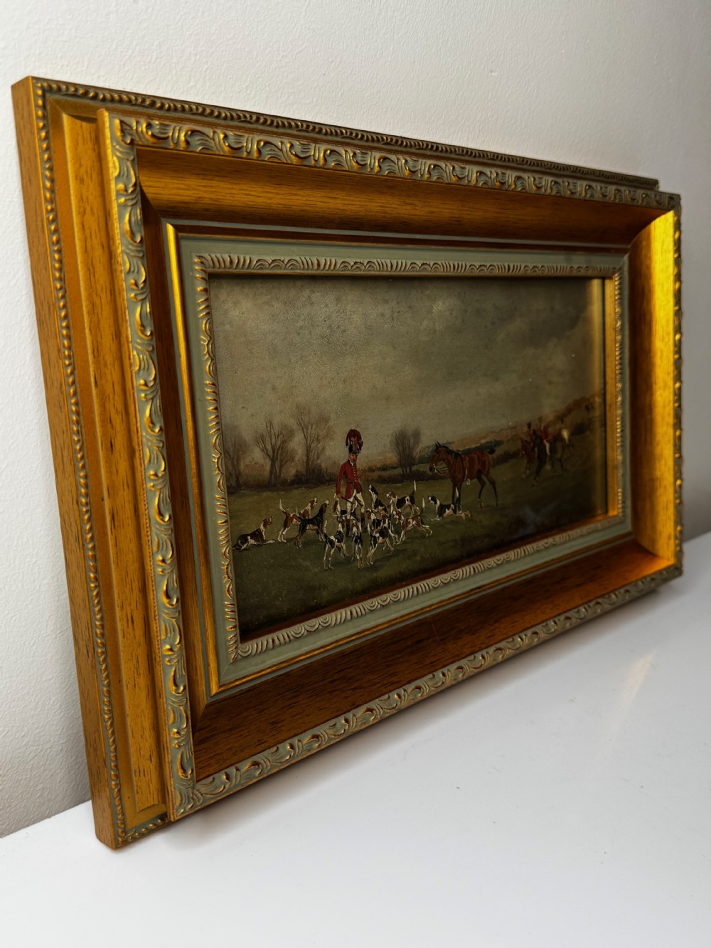 A Victorian oil painting depicting a fox hunting scene with huntsmen on horseback and a pack of hounds in a countryside landscape, housed in a gilded frame. View V