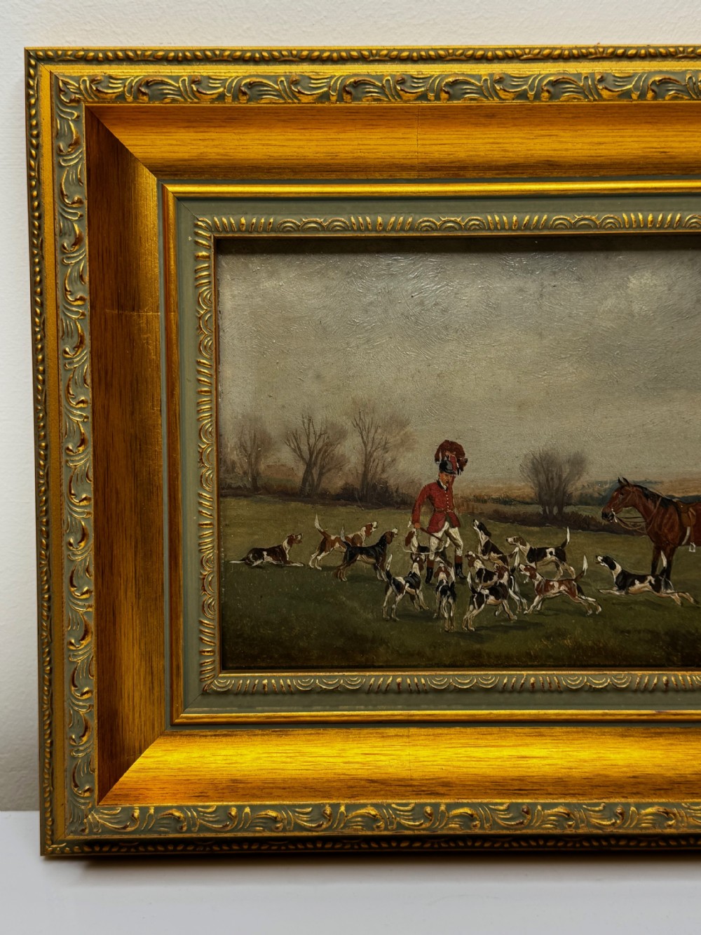 A Victorian oil painting depicting a fox hunting scene with huntsmen on horseback and a pack of hounds in a countryside landscape, housed in a gilded frame. View VI
