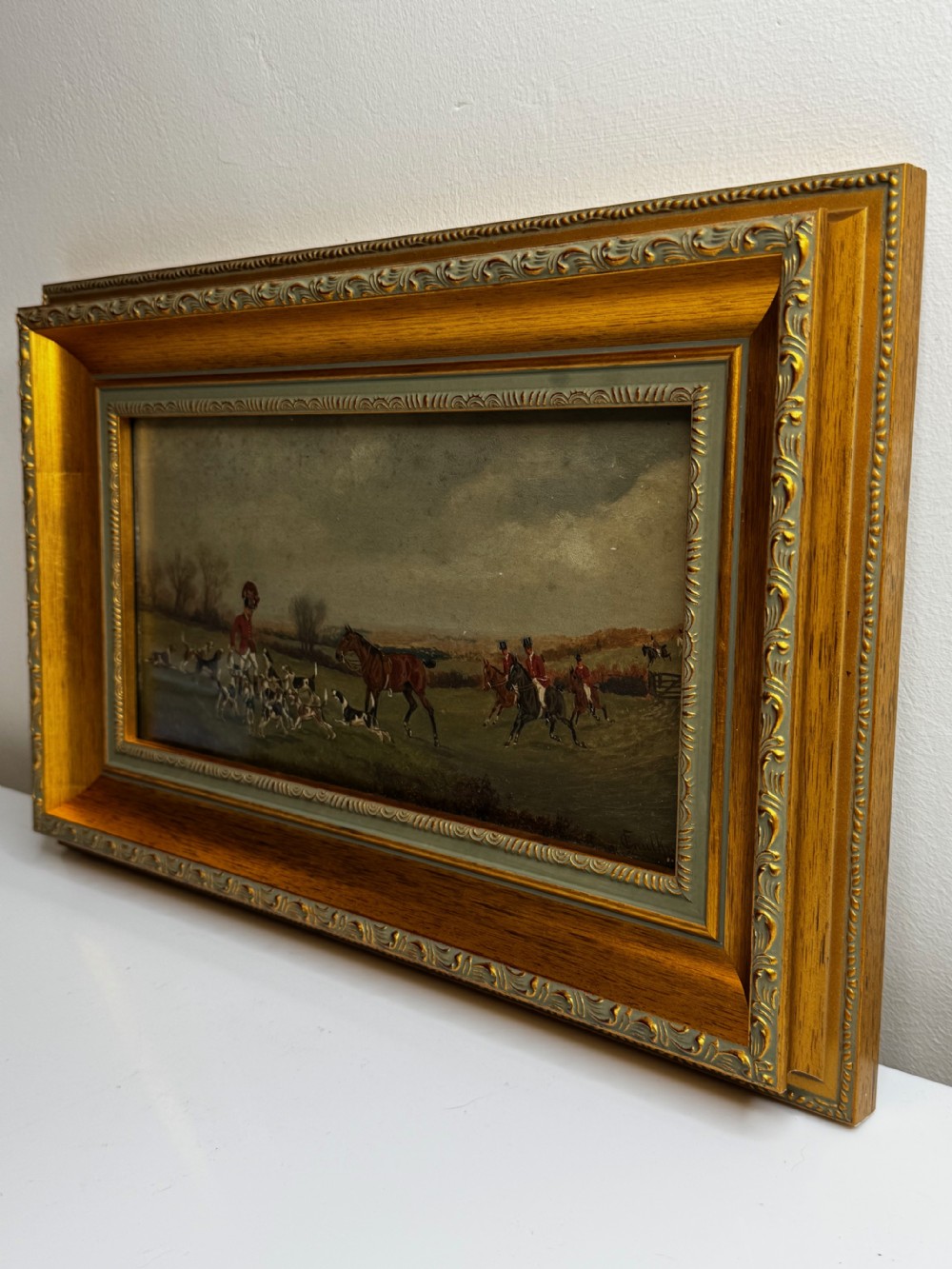 A Victorian oil painting depicting a fox hunting scene with huntsmen on horseback and a pack of hounds in a countryside landscape, housed in a gilded frame. View IX