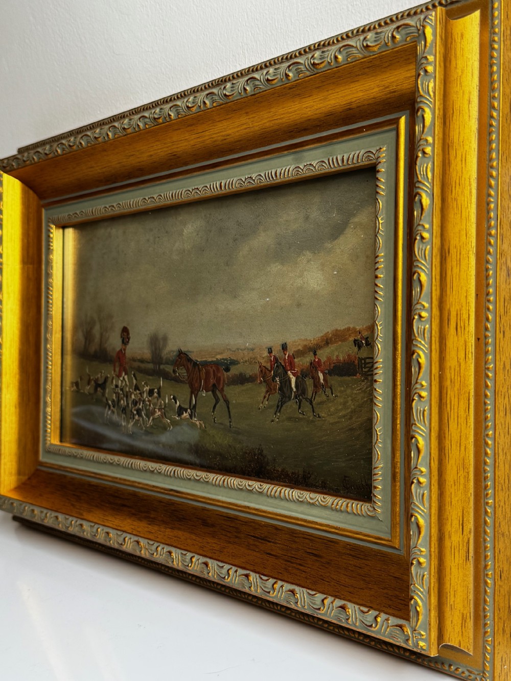 A Victorian oil painting depicting a fox hunting scene with huntsmen on horseback and a pack of hounds in a countryside landscape, housed in a gilded frame. View X