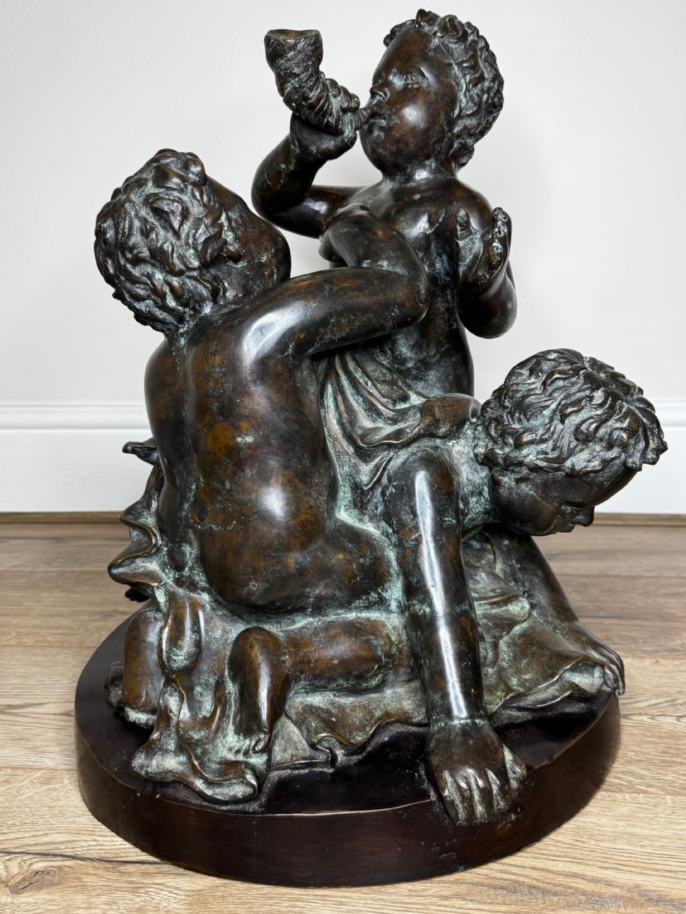 A dark patinated French bronze sculptural group depicting three putti playing, with one child blowing into a conch shell. View III