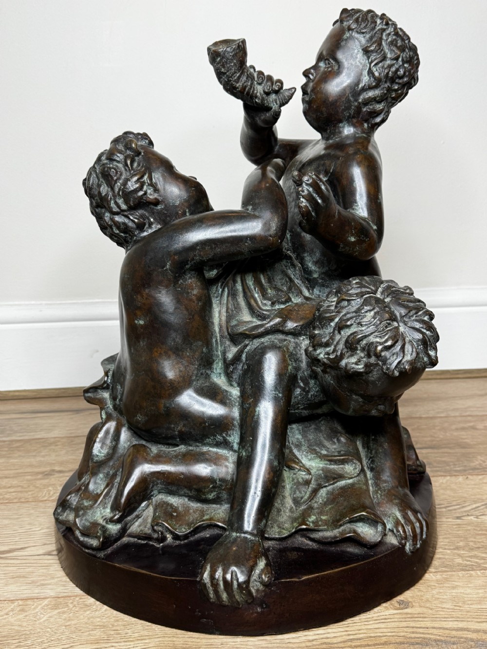 A dark patinated French bronze sculptural group depicting three putti playing, with one child blowing into a conch shell. View XVIII