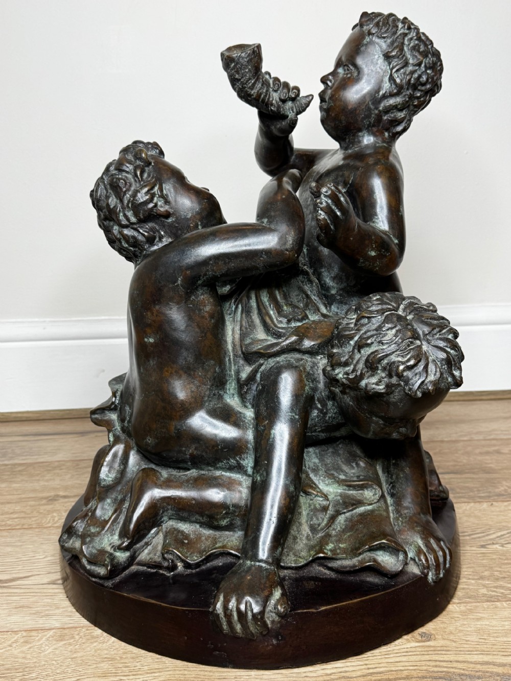 A dark patinated French bronze sculptural group depicting three putti playing, with one child blowing into a conch shell. View XIX