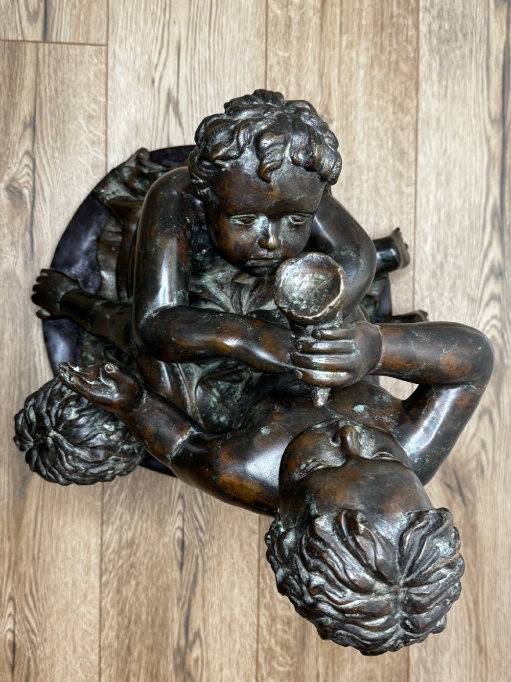 A dark patinated French bronze sculptural group depicting three putti playing, with one child blowing into a conch shell. View XXII