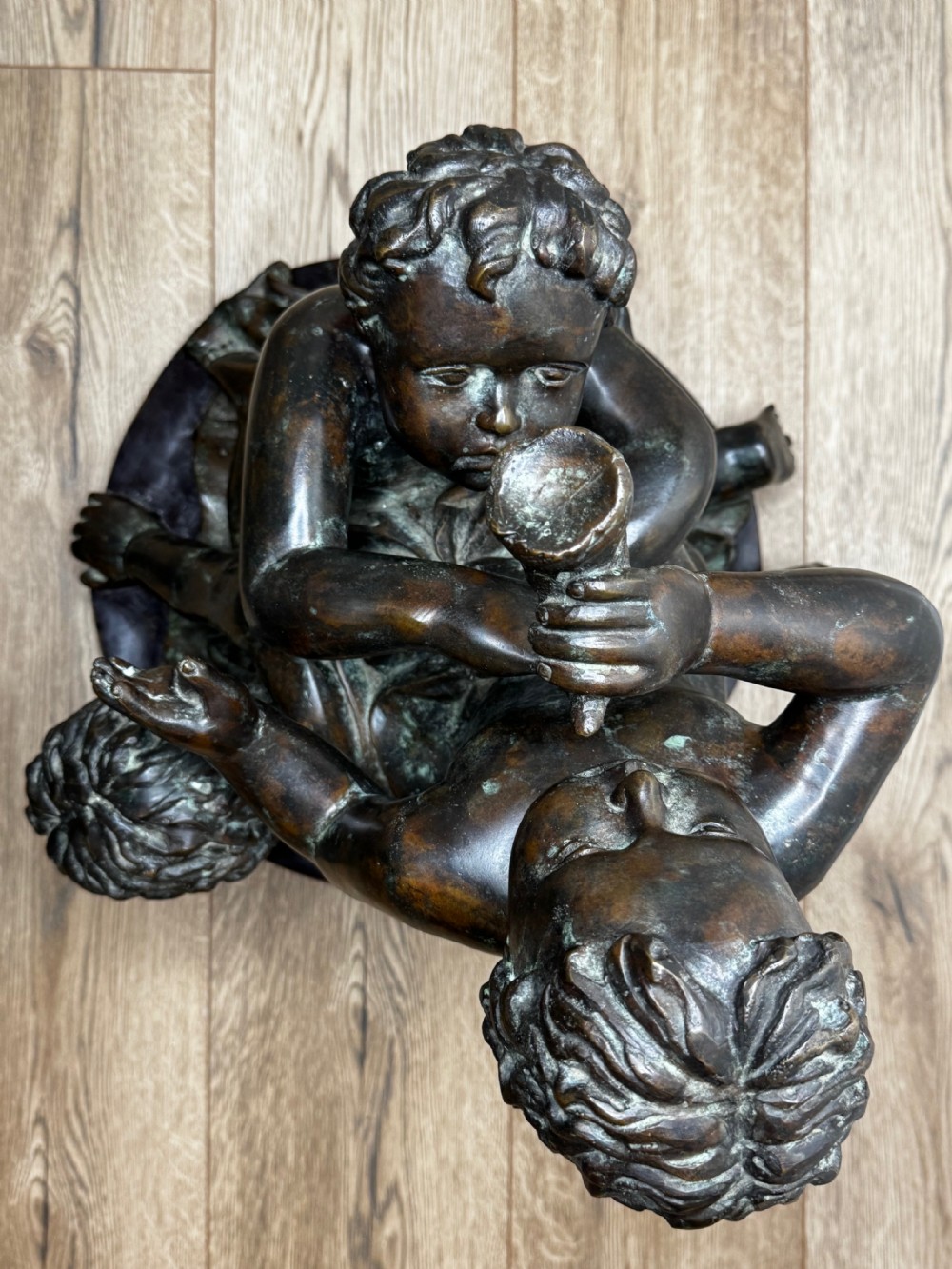 A dark patinated French bronze sculptural group depicting three putti playing, with one child blowing into a conch shell. View XXIII